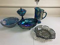 Full set of five blue iridescent carnival glass pieces shown from the front with clear light background