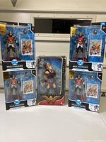 Four DC Multiverse Wonder Woman action figures, packaged with Green Lantern cards, and one boxed Barbie Black Label Wonder Woman doll centerpiece.