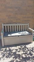 Front view of beige plastic outdoor storage bench featuring slatted backrest and padded seat cushion.