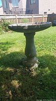 Full view of the concrete bird bath outside on grass, showing basin and pedestal.