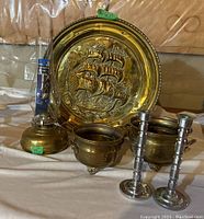 Lot showing brass oil lamp with glass hurricane shade, brass embossed wall plate with sailing ship design, two brass planters, and two stainless steel candlesticks.