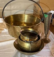 Photo showing a large brass pot with a handle, a hammered brass bowl, and a smaller brass container with a lid and base bowl