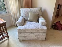 Full view of Simmons upholstered armchair with cushion in living room corner, showing light-colored floral fabric upholstery and included pillows.
