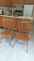 Photo showing three wooden dining chairs with spindle backs and turned legs, placed near a kitchen counter.