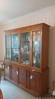 Full front view of the two piece china cabinet showing the hutch with glass doors and displayed china, and the buffet with four doors below.