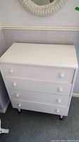 Front view of the white painted plywood dresser showing four drawers with round wooden knobs.