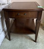 Front view showing drawer with brass handle and carved tapered legs.
