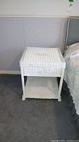 Front view of white painted wicker end table with one drawer, showing squared shape and chipped paint.