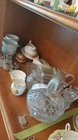Photo showing white china cups, cut glass trays, glass lidded bowl with pinwheel design, and cream and sugar sets.