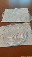 Two round glass platters and one large leaf-shaped glass divided serving dish placed on a white textured cloth on wooden surface.