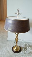 Full view of table lamp showing brass finish base with brown cardboard shade, gold trim, and wood base.