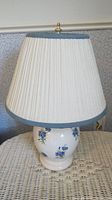 Front angled view of the ceramic lamp showing the floral design and pleated fabric shade with blue trim.