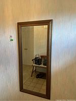 Full view of the framed wall mirror hanging vertically on the wall showing its reflective glass and carved wooden frame.