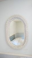 Full front view of the oval mirror hung on a wall reflecting a bedroom corner.