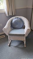 Front view of the white painted wicker rocking chair with light blue cushions showing the seat and decorative pillow.