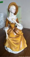 Front view of Royal Doulton figurine, detailing face, dress, and hat.