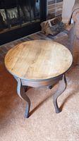 Full view of wood side table with natural round top and three curved legs in a rustic finish.