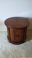 Front view of the round wooden drum side table showing the door panels and handles.