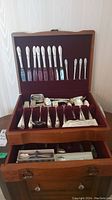 Full view of the silver plated cutlery set inside a wooden box with velvet lining, showing knives, forks, spoons, and other utensils arranged in upper and lower compartments and a drawer below.