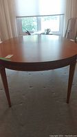 View of the wood dining table from side showing the round shape and four tapered legs, wood finish with scratches.