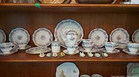 Full display of the EB Foley Cornflower tea set including plates, cups, saucers, teapot, cream, sugar, and Adderley flower figurines arranged on a wooden shelf.