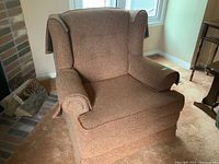 Full view of brown wingback chair showing fabric and general shape, positioned near a fireplace.