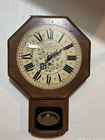 Front view of vintage New England wooden wall clock showing octagonal wood frame, Roman numeral dial with floral center, winding key attached.