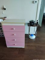 Front angled view of a pink and white chest with four drawers and white knobs, showing some minor wear at the bottom.