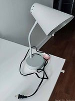 White conical shade desk lamp with round metallic base and black cord on white surface