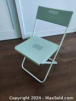 Green folding metal chair placed on wooden floor against white wall