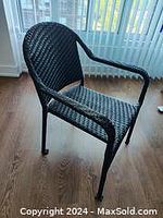 Photo showing a black woven synthetic armchair on a hardwood floor near a window with vertical blinds.