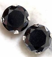 Close-up of one black moissanite round faceted earring held by a four-prong 10K gold setting.