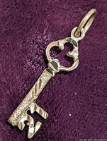 Photo showing close-up of 10K yellow gold key pendant with textured and polished surfaces on a purple fabric background.