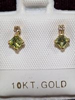 Close-up of pair of 10K gold earrings with peridot and diamond stones on white earring display stand.