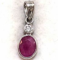 Close-up front view of a 14K gold pendant featuring an oval faceted ruby and a round diamond above it.