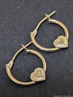 Pair of yellow gold hoop earrings each with a heart detail, shown on a black background.