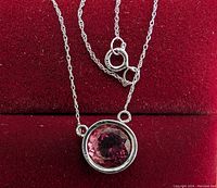 Pendant and chain displayed on red velvet background showing bezel set round pink gemstone