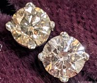 Close-up of two round light brown diamonds in four-prong gold settings on burgundy background