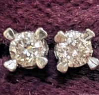 Close-up front view of both diamond stud earrings against dark fabric backdrop showing cut and prong details.