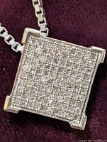 Front view of square diamond pavé pendant on box chain against burgundy background