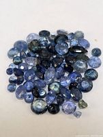 Loose sapphires of mixed cuts and sizes laid out on a white background showcasing various shades of blue.