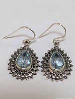 Front view of the sterling silver blue topaz earrings showing the pear-shaped stones and detailed silver halo setting.