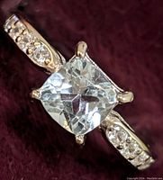 Close-up front angled view of sterling silver ring with cushion-cut blue topaz center stone and cubic zirconia accent stones on band.