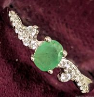 Close-up of sterling silver ring with an oval green emerald center stone and clear cubic zirconia accents on a purple background