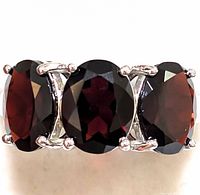 Close-up front view of sterling silver ring with three faceted deep red garnet oval stones.