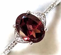 Close-up view of the sterling silver ring showing the oval garnet gemstone, cubic zirconia side stones, and detail of the band.