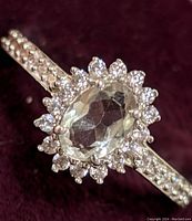 Close-up front view of the ring showing the oval green amethyst center stone surrounded by clear stones and the decorated band.