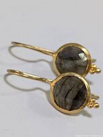 Close-up of pair of yellow gold-toned sterling silver earrings with round faceted labradorite stones in bezel setting and small decorative beads.
