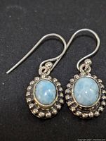 Close-up photo of the pair of sterling silver larimar earrings with light blue oval stones and beaded silver border, on black background.
