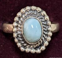 Close-up of front face of sterling silver ring showing oval cabochon larimar gemstone with beaded silver bezel and twisted rope design.
